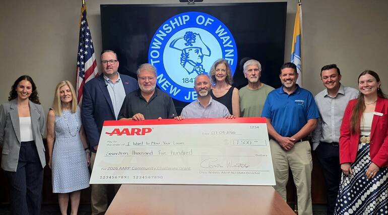 Brian Schwartz stands with Wayne Township officials, AARP New Jersey staff and volunteers in the township municipal chambers, holding an oversized AARP Community Challenge Grant check.