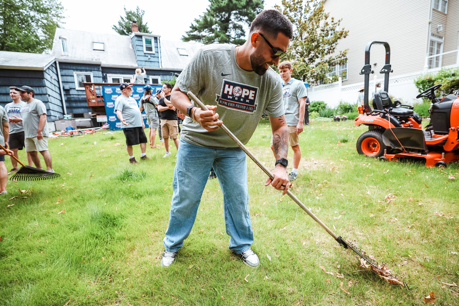 Ali Sanchez rakes cut grass across the lawn while other volunteers and an orange mower stand behind him.