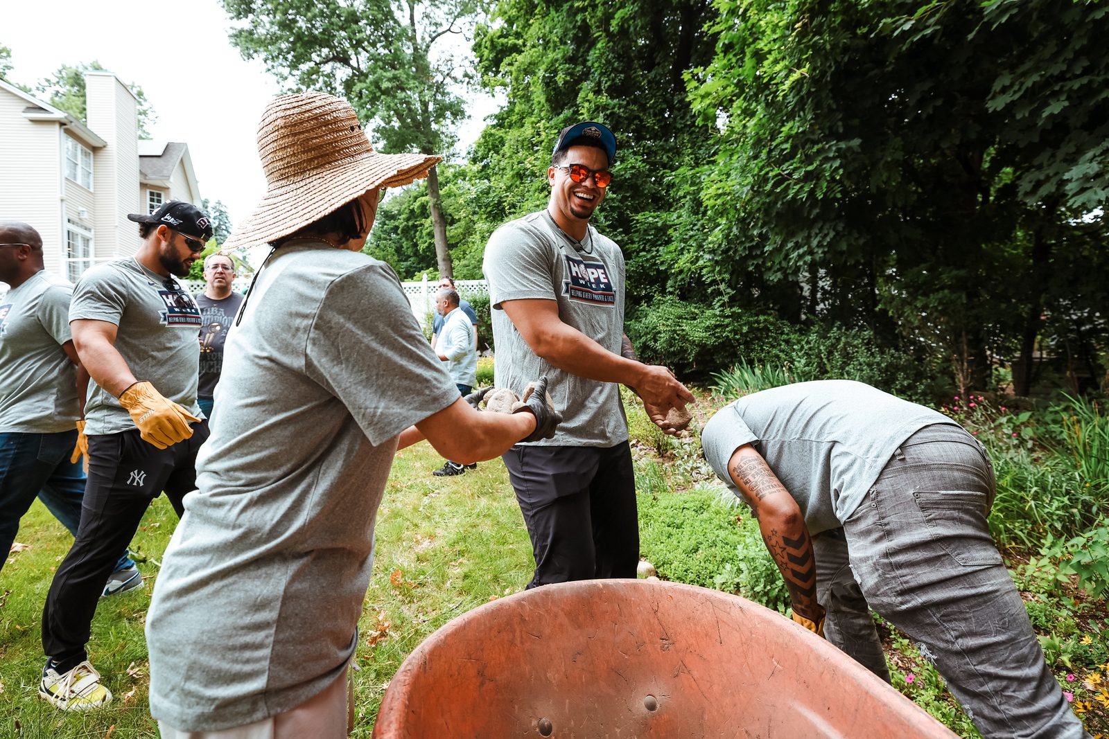 Volunteers form a line to pass garden stones hand to hand, with a wheelbarrow in the foreground.