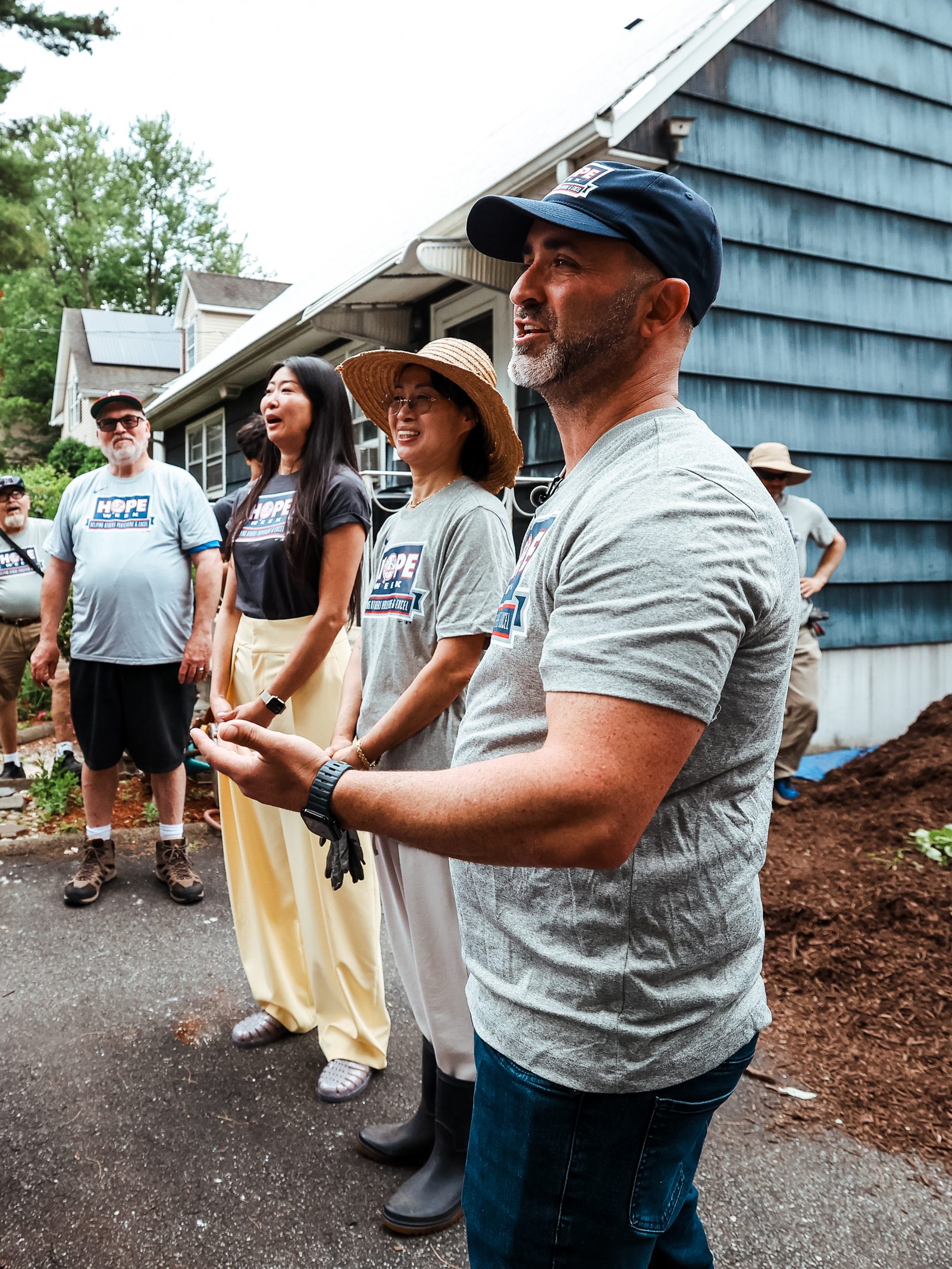 I Want To Mow Your Lawn founder Brian Schwartz, in a cap and HOPE Week T-shirt, stands with a group of volunteers beside the house.